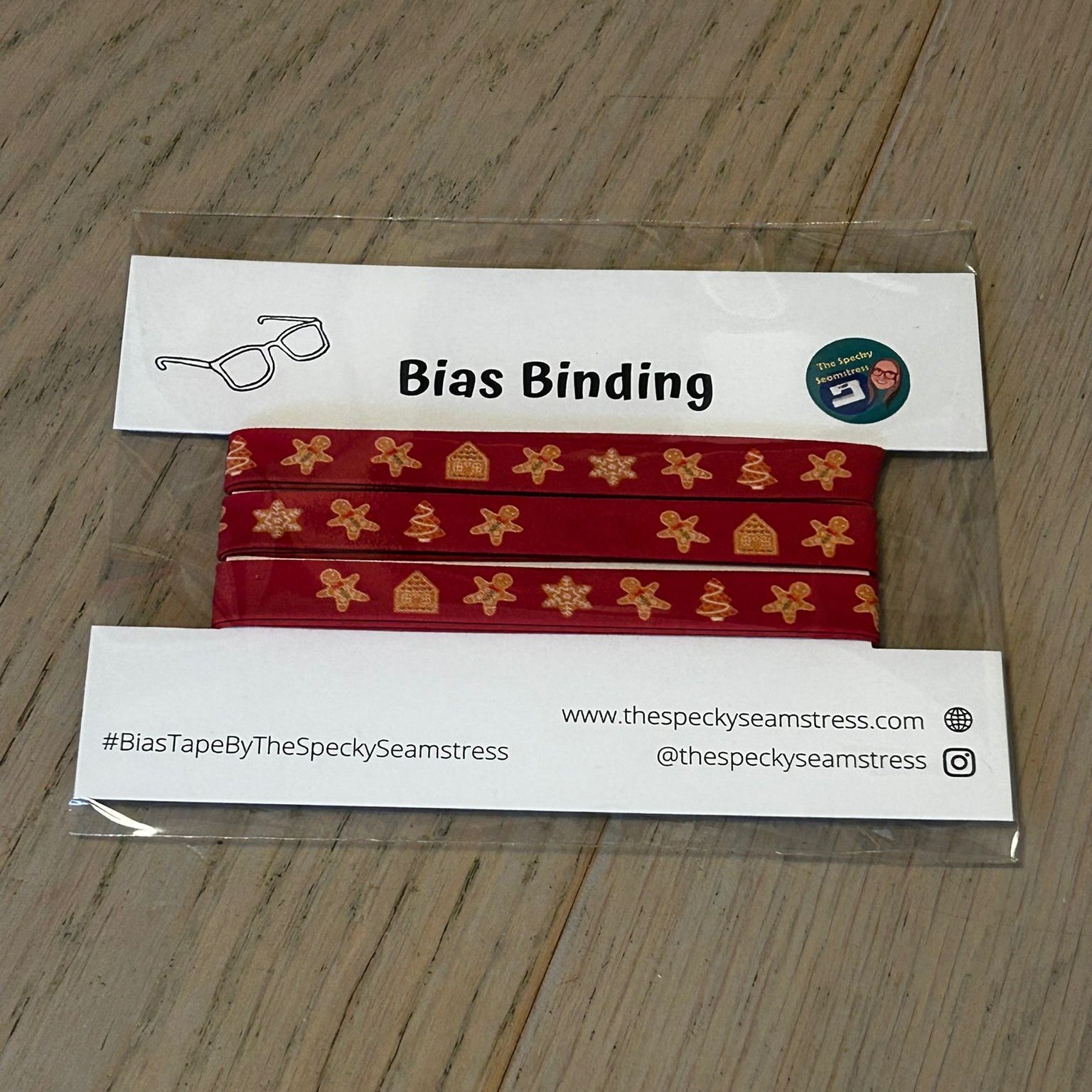 Red bias binding with gold patterns on a branded card, displayed on a wooden surface.