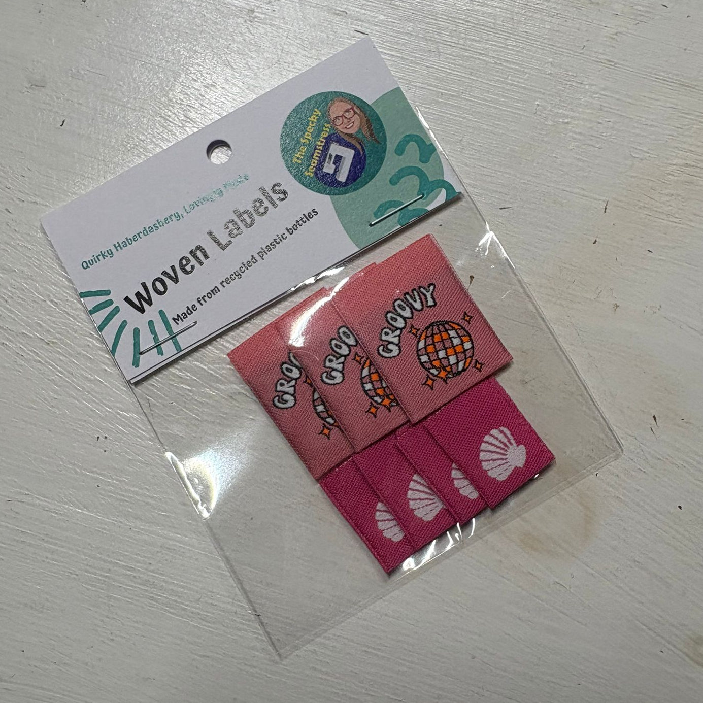 Two different styles of pink woven labels with cartoon designs in a clear plastic bag.