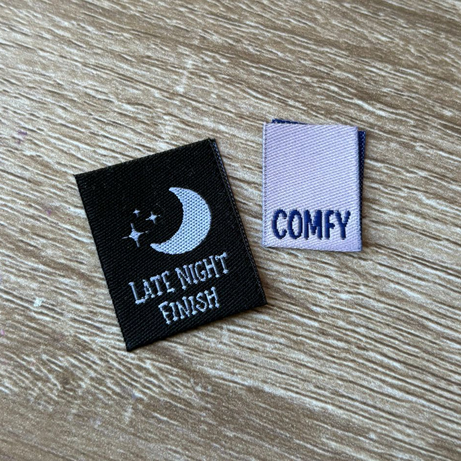 Two small labels on a wooden surface, one with 'Late Night Finish' text and moon design, the other with 'COMFY' text.