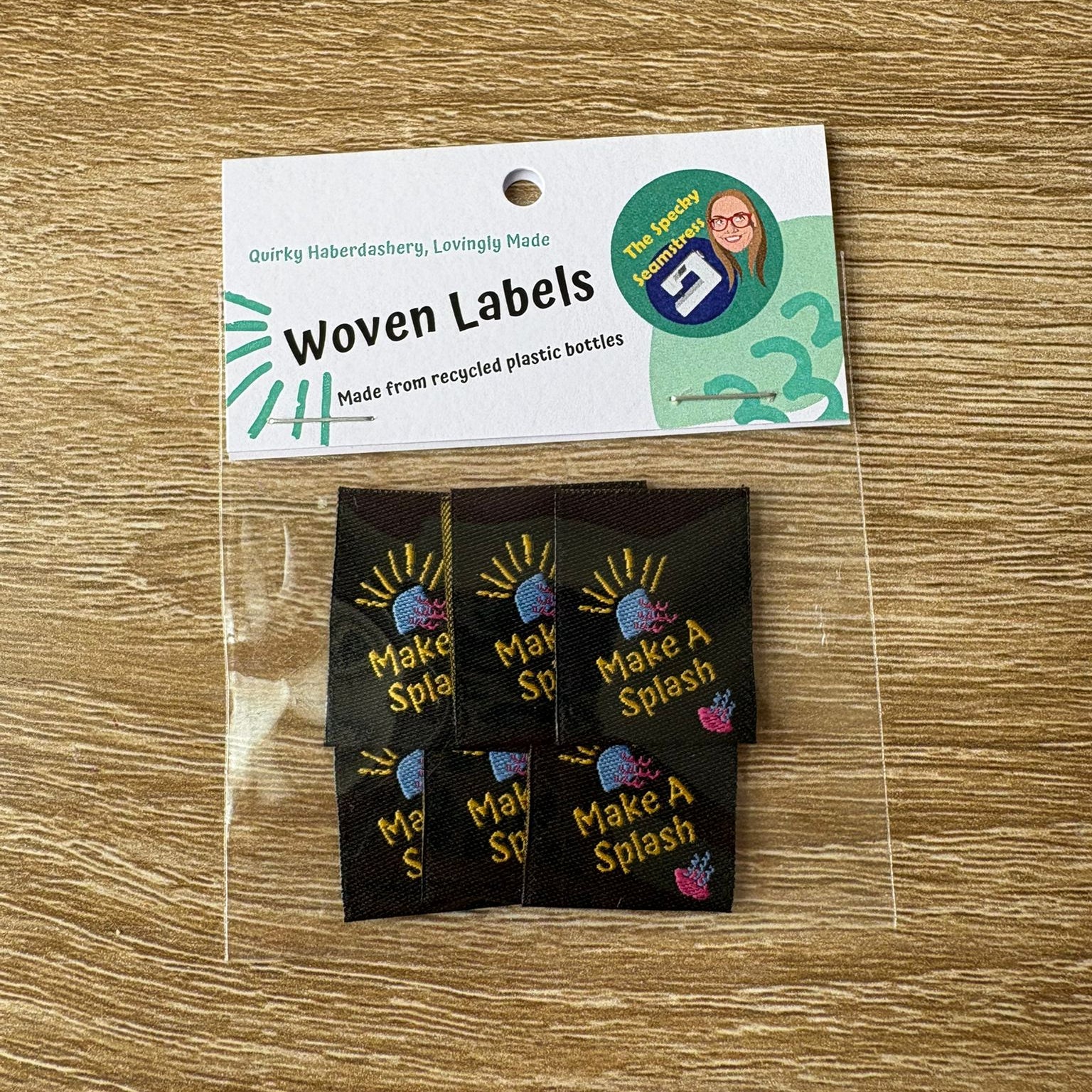 Woven labels with 'Make a Splash' design on a wooden surface