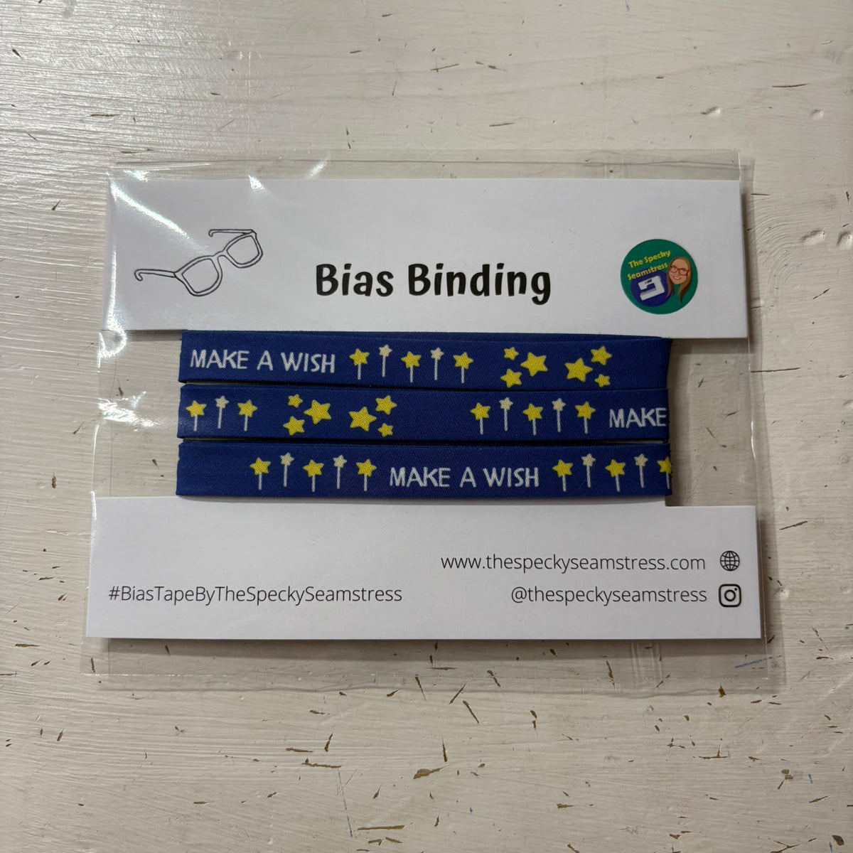 Blue 'Make A Wish' bias binding with yellow stars and wands, packaged in a clear plastic sleeve with a white paper header card labeled 'Bias Binding'.