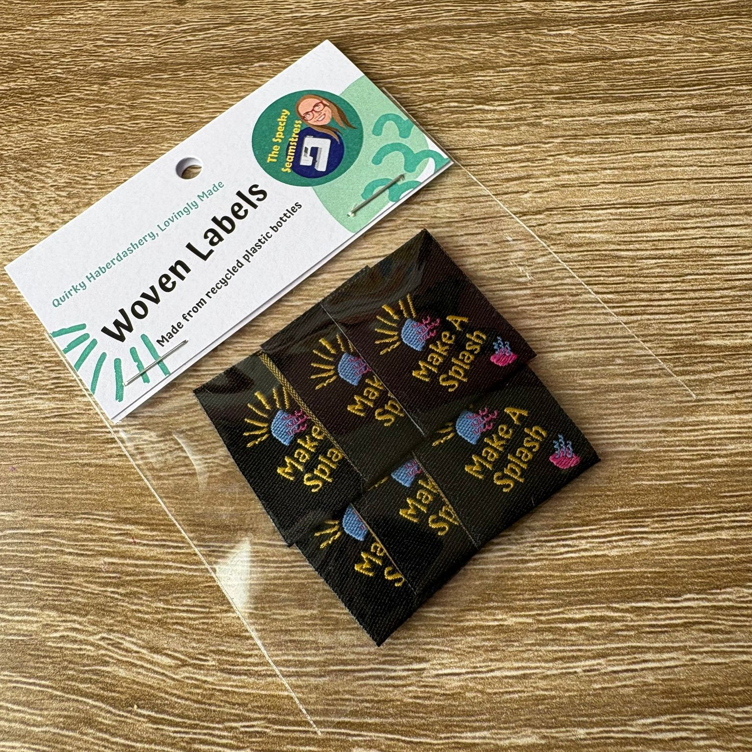 Woven labels on a wooden surface with a label packaging in the background.