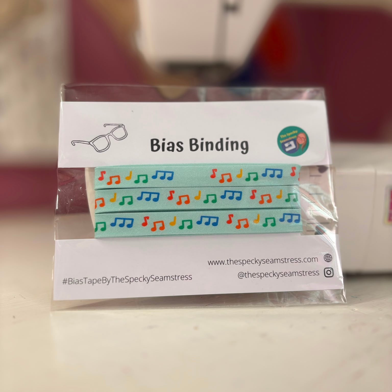 Bias binding tape with a colorful music note pattern, packaged in a clear plastic sleeve on a white display card labeled 'Bias Binding' by The Specky Seamstress.