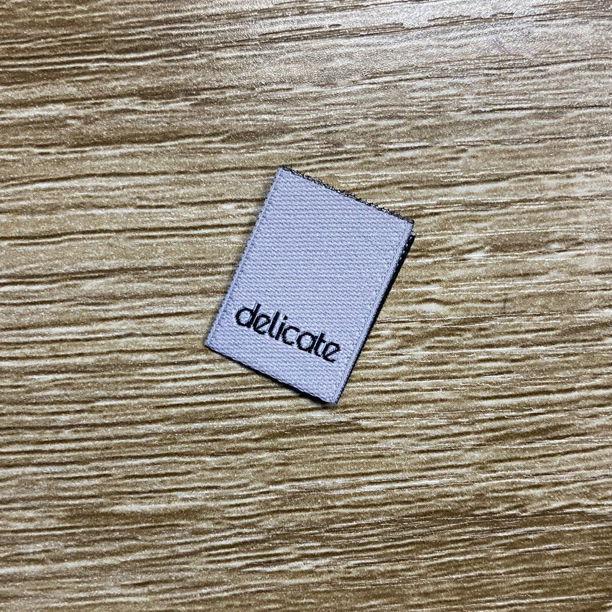 'Delicate' woven label on a wooden surface