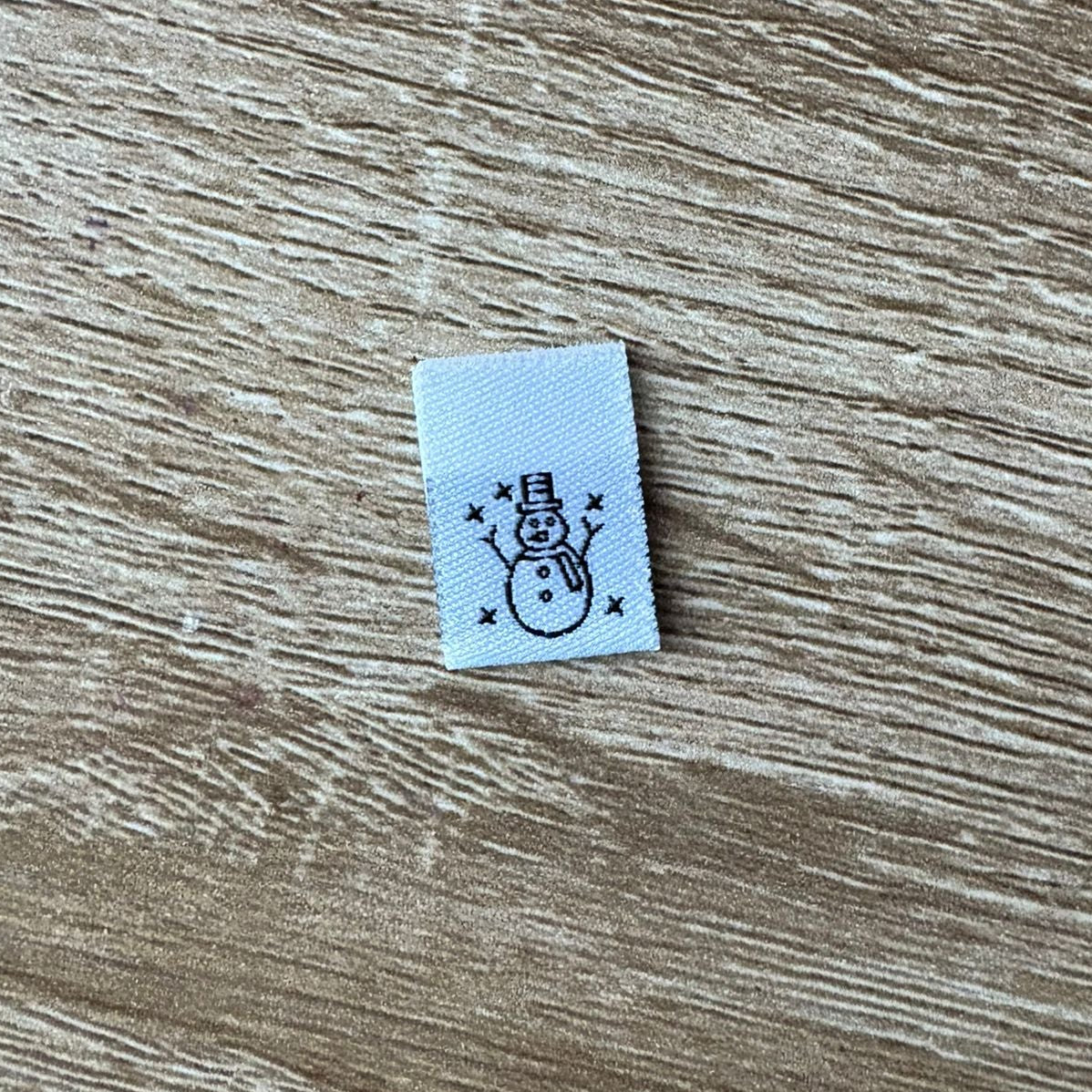 Small white label with a snowman design on a wooden surface