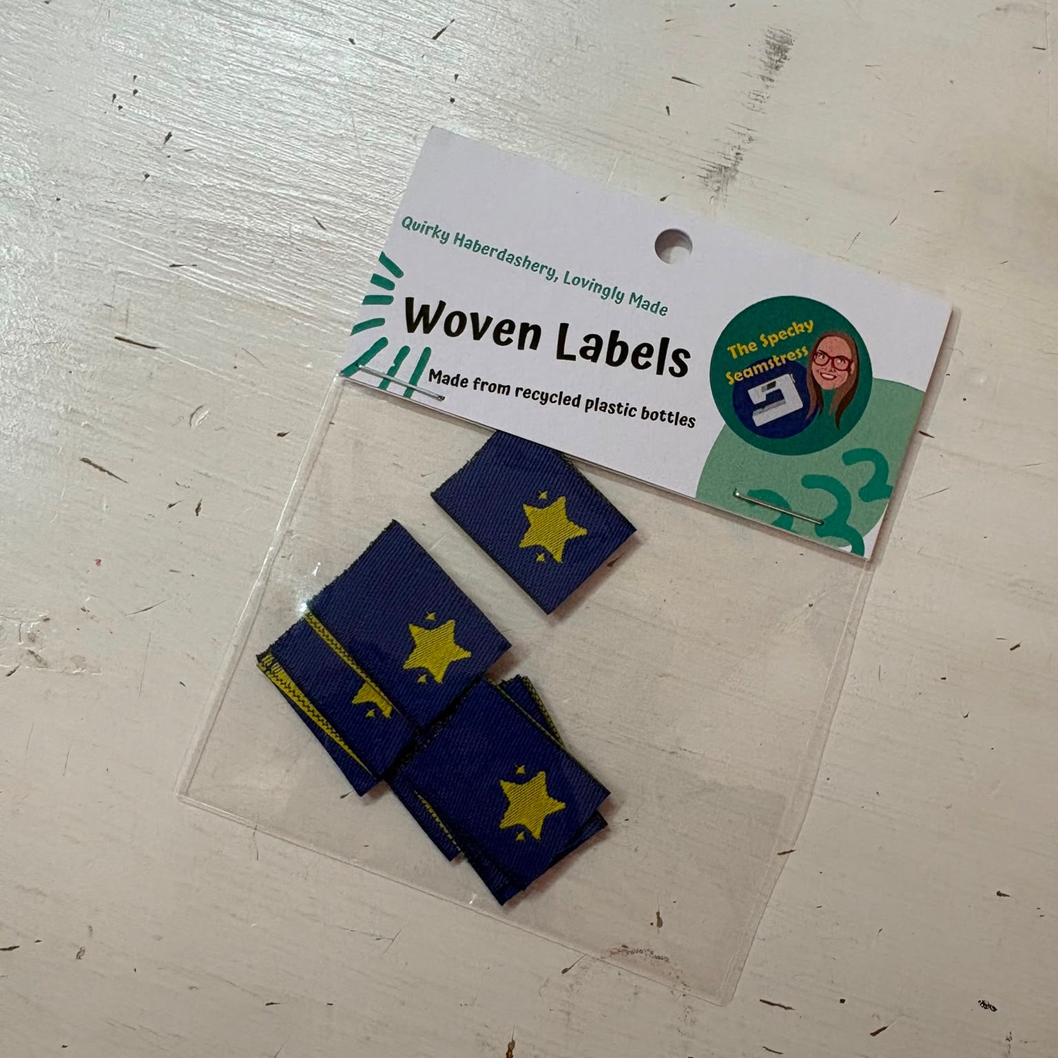 Eight small woven labels in dark blue with yellow star designs, packaged in a clear plastic bag with a white paper header card.