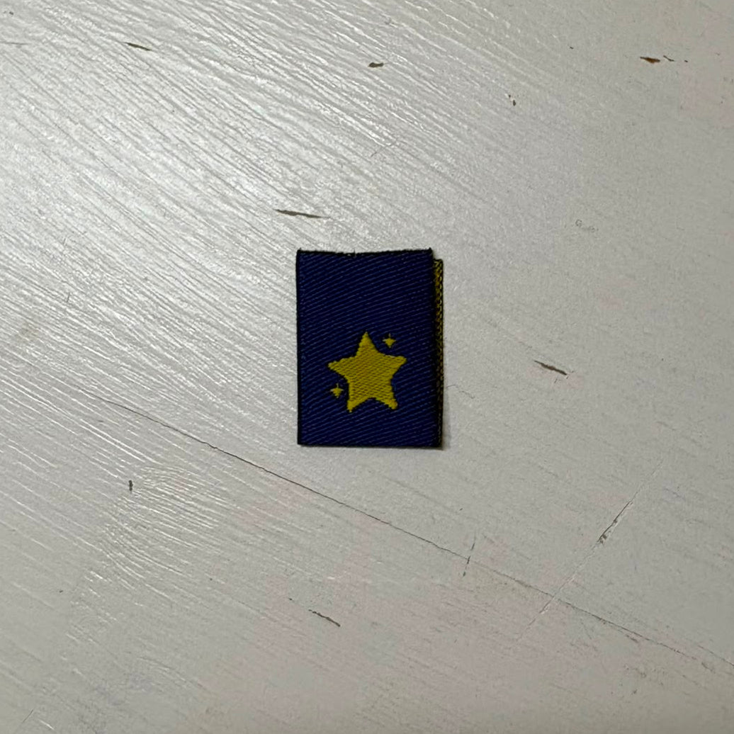 A mini navy blue woven with a yellow star, placed on a light-coloured wooden surface.
