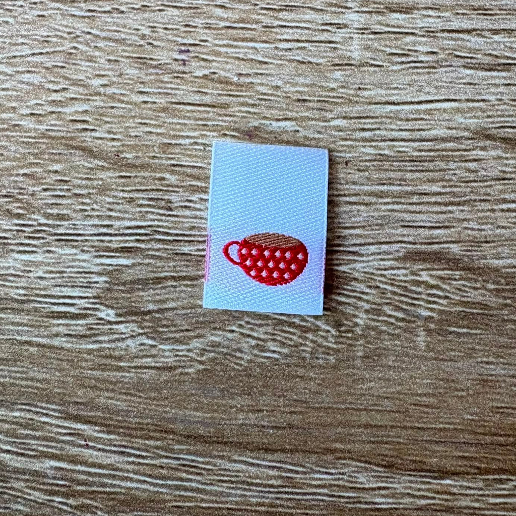 Mini woven label with a red and teacup  design on a wooden surface