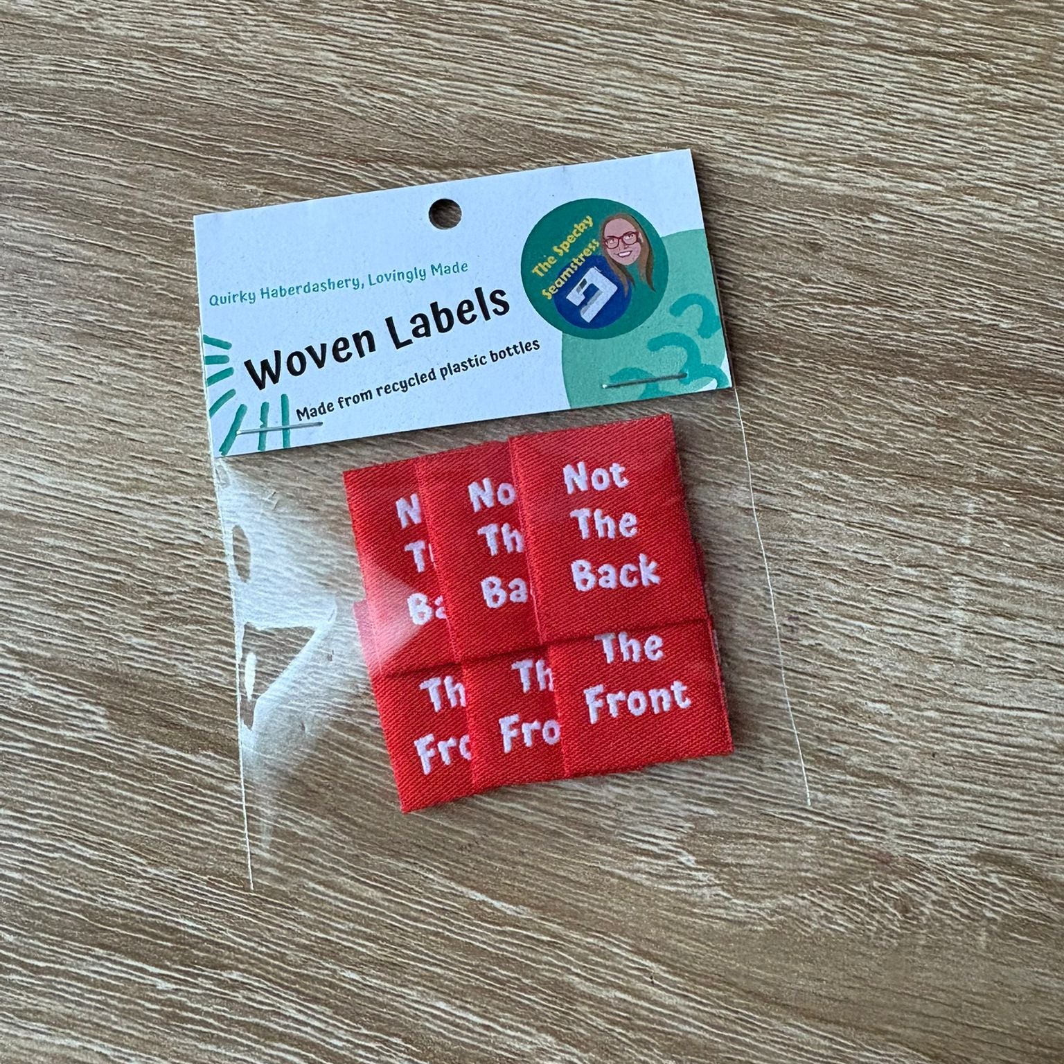 Red woven labels with text in a clear bag on a wooden surface.
