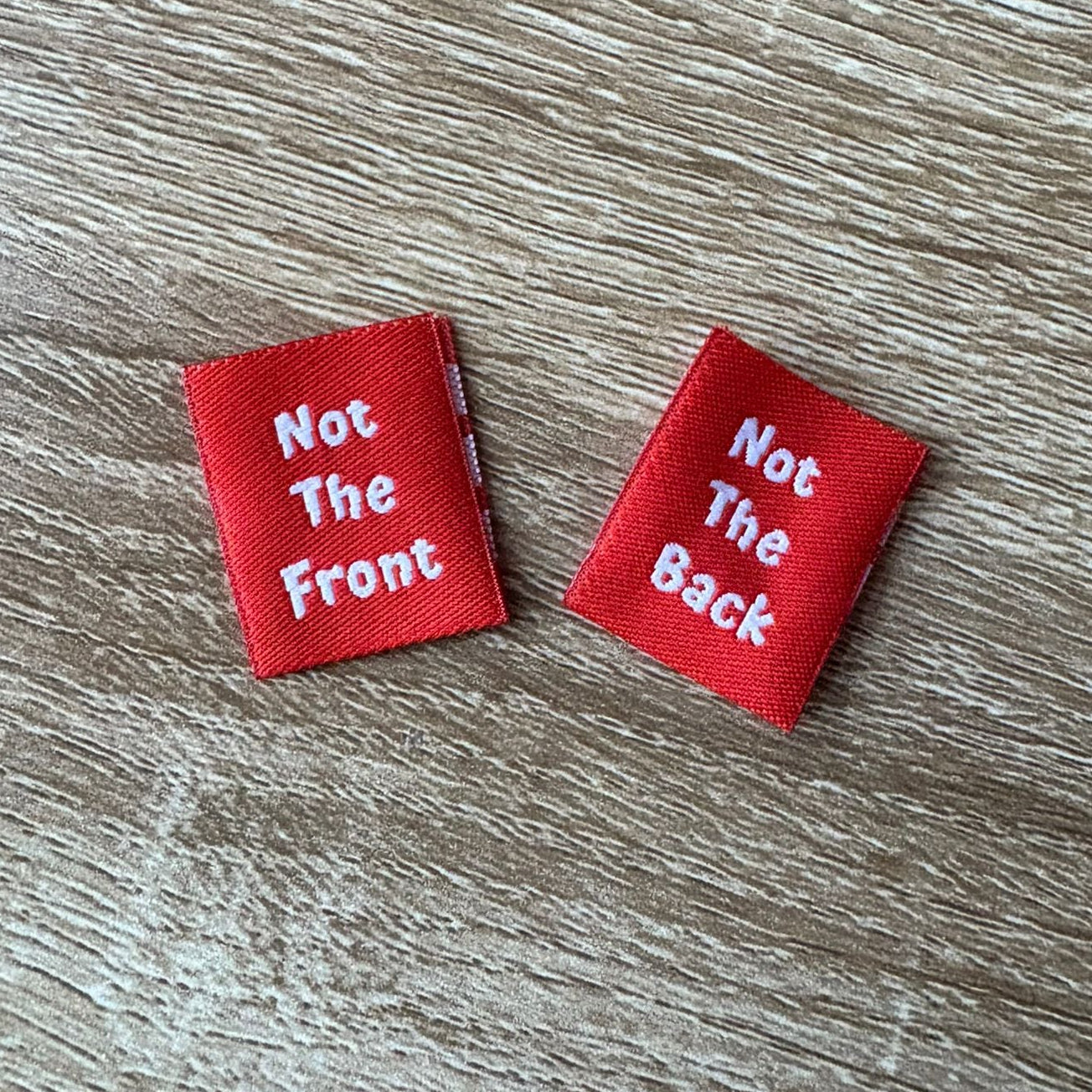 Two red labels with white text on a wooden surface; one label shows the front, one label shows the reverse. 