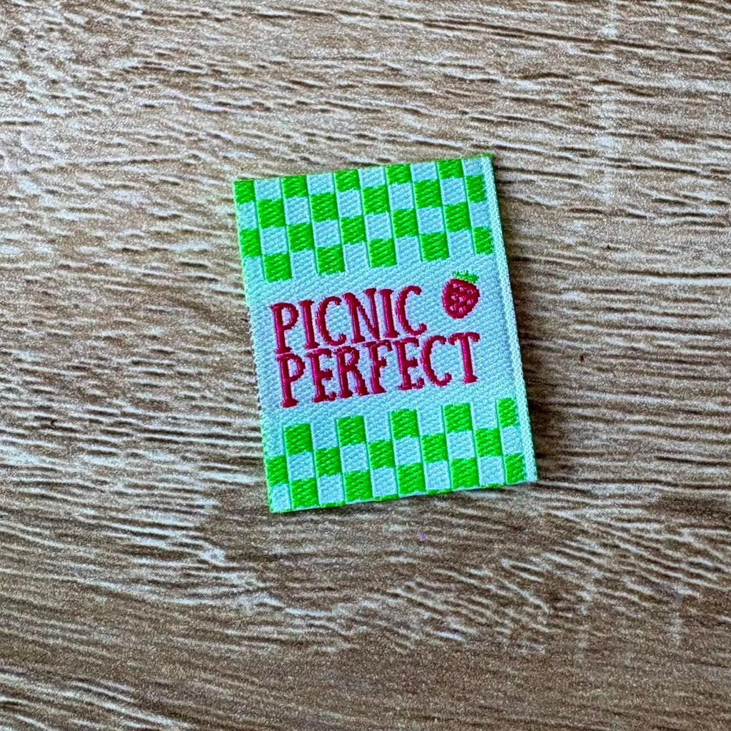 Woven label with 'Picnic Perfect' text on a checkered background, placed on a wooden surface.