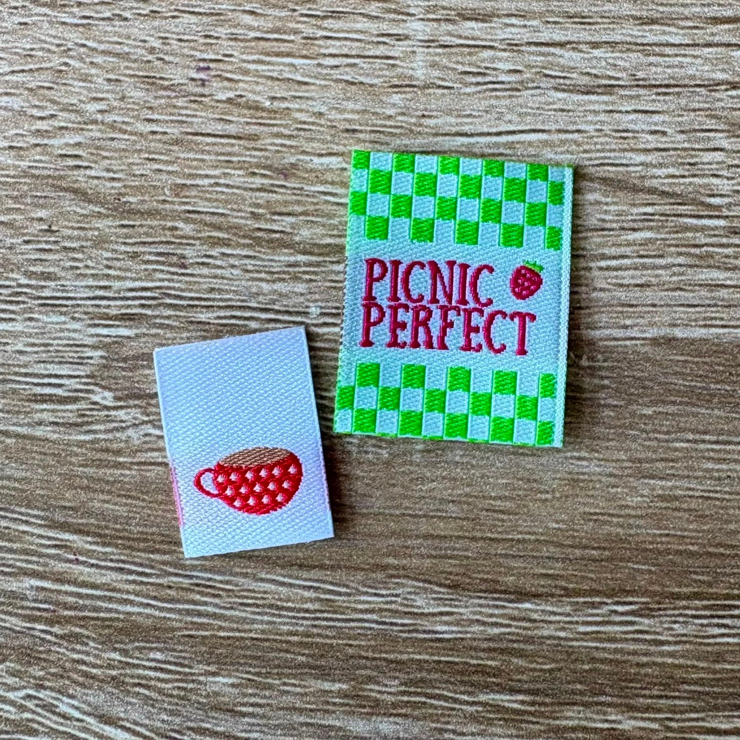 Two woven labels on a wooden surface, one with a red teacup design and the other with 'Picnic Perfect' text.