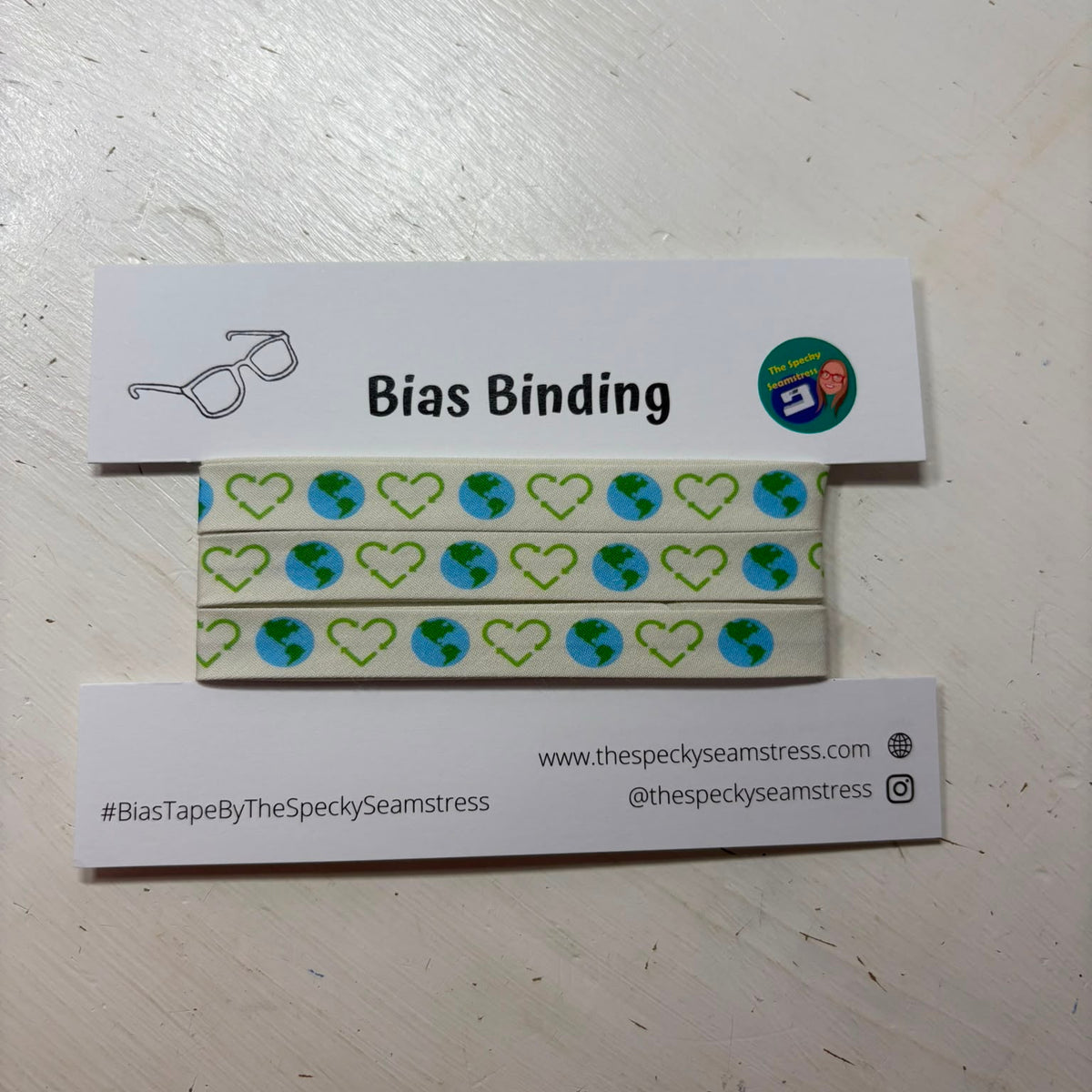 A package of Planet Recycle bias binding on a white backing card on a painted wooden surface. 