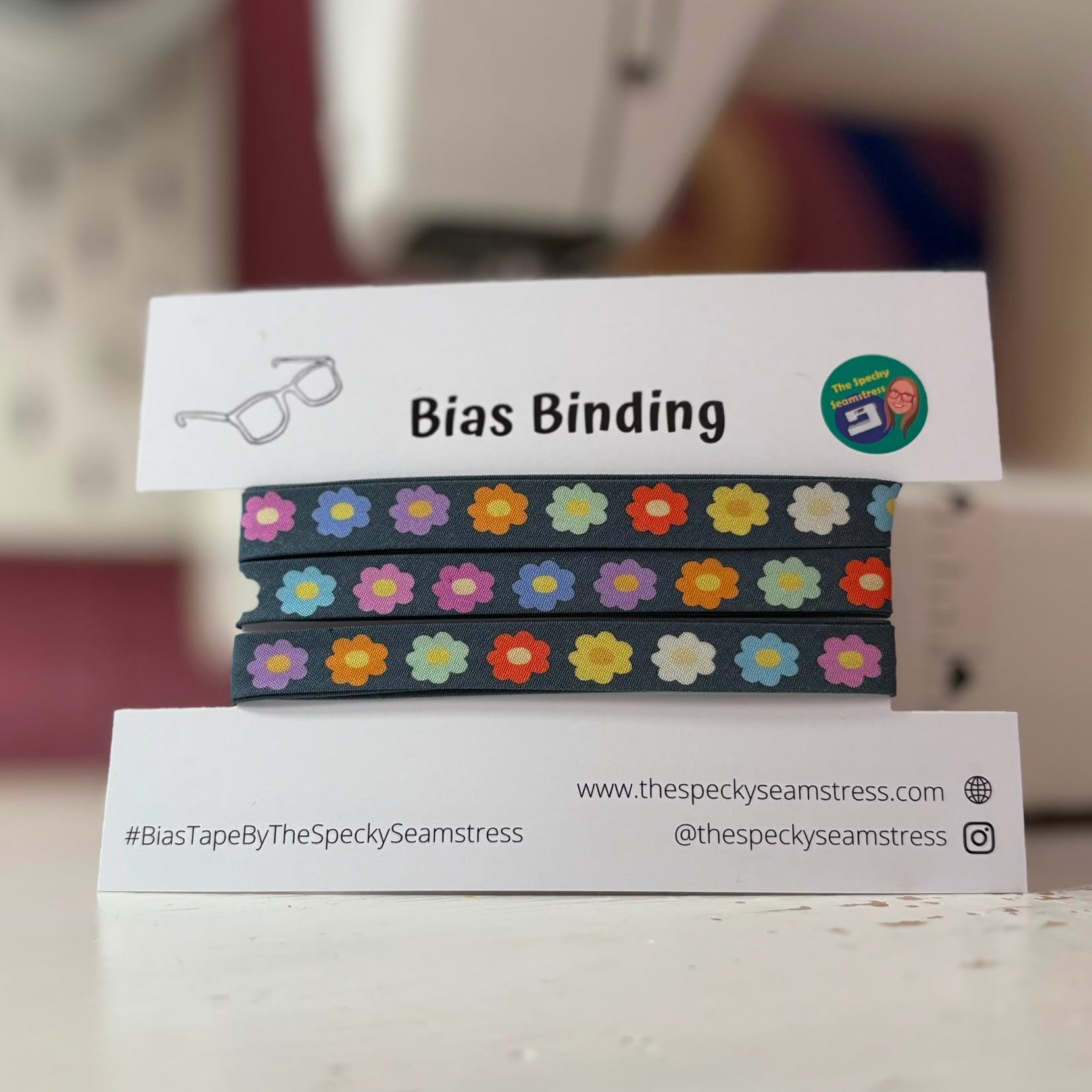 A pack of bias binding with a branded label in front of a sewing machine.