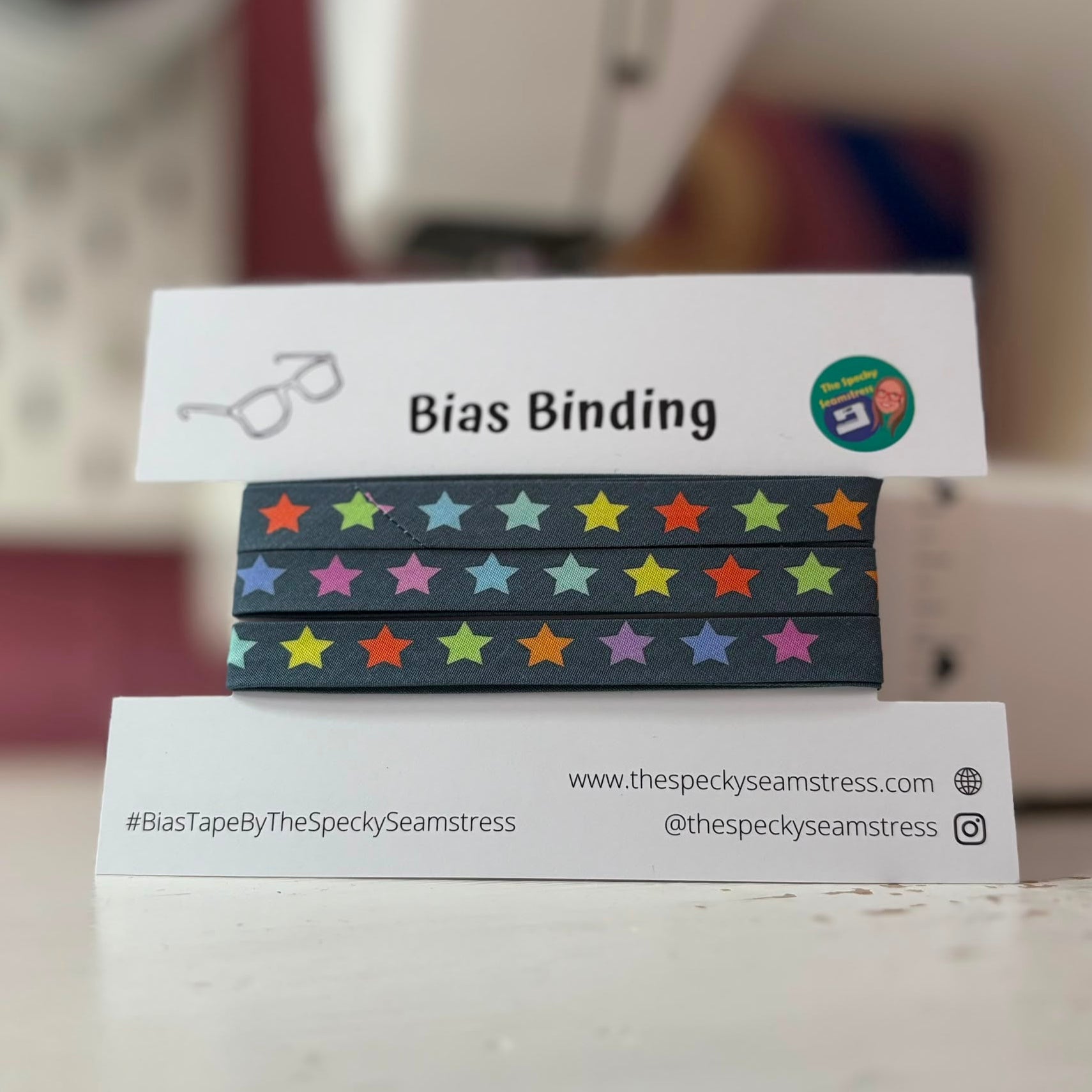Bias binding with colorful star pattern on a branded card in front of a sewing machine.
