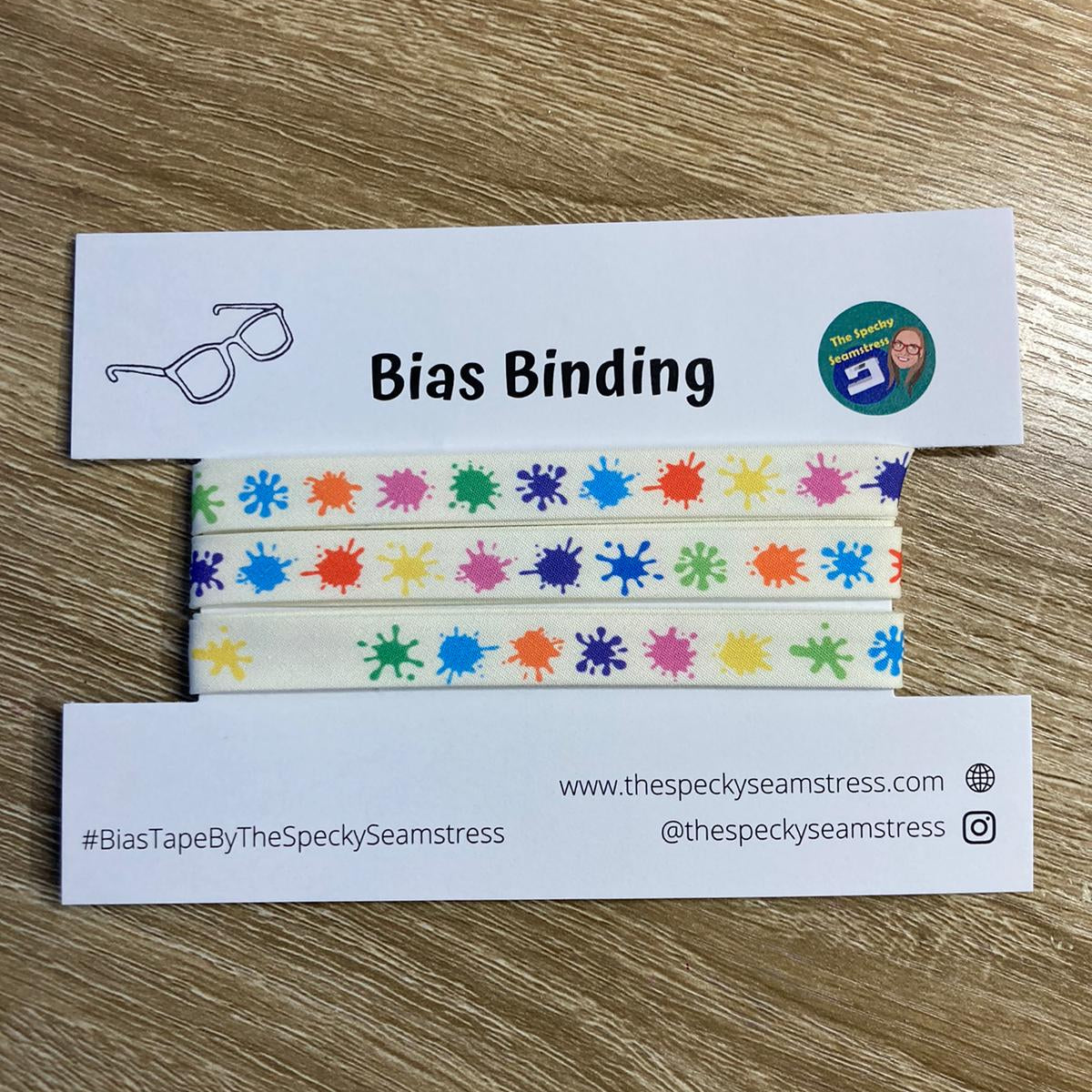 Splat multi-coloured bias binding wrapped on a backing card on a wooden background.