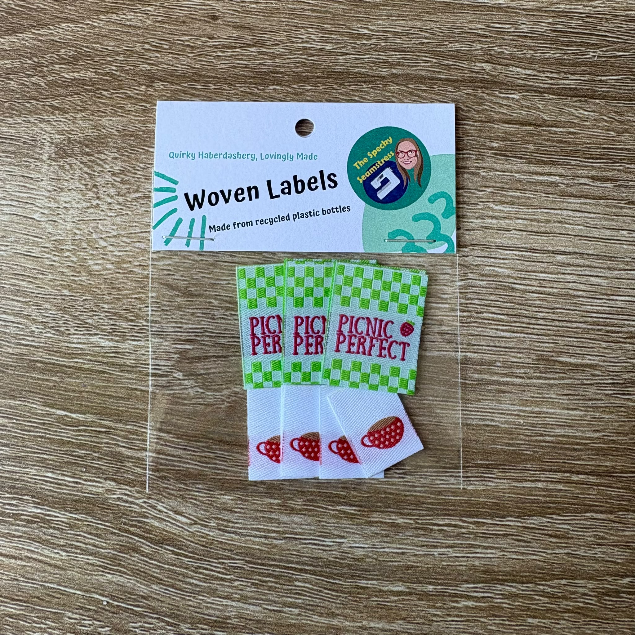 3 woven labels with 'Picnic Perfect' and 4 Mini labels with Teacups in a packet on a wooden surface.