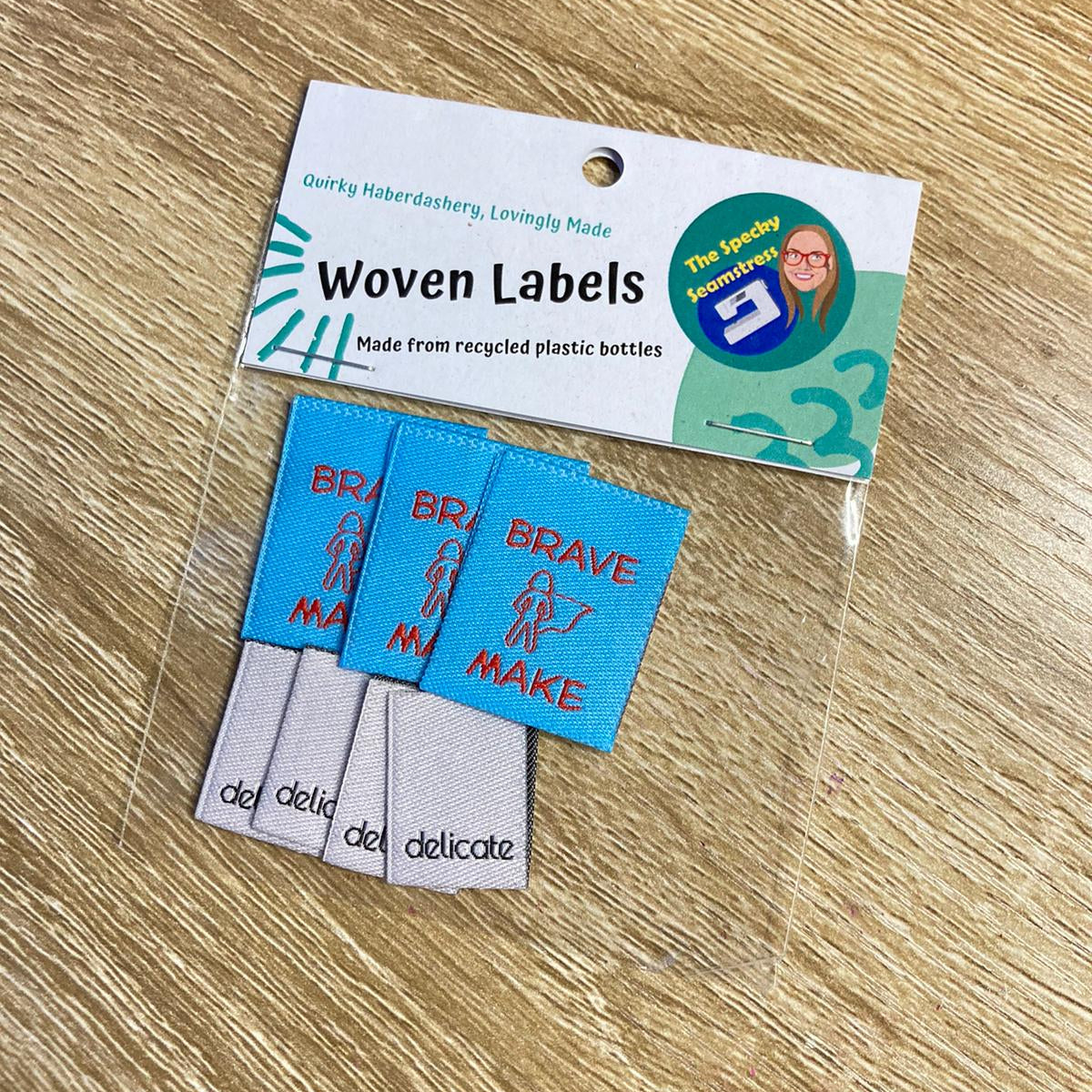 7 Woven labels with text on a clear bag, placed on a wooden surface.