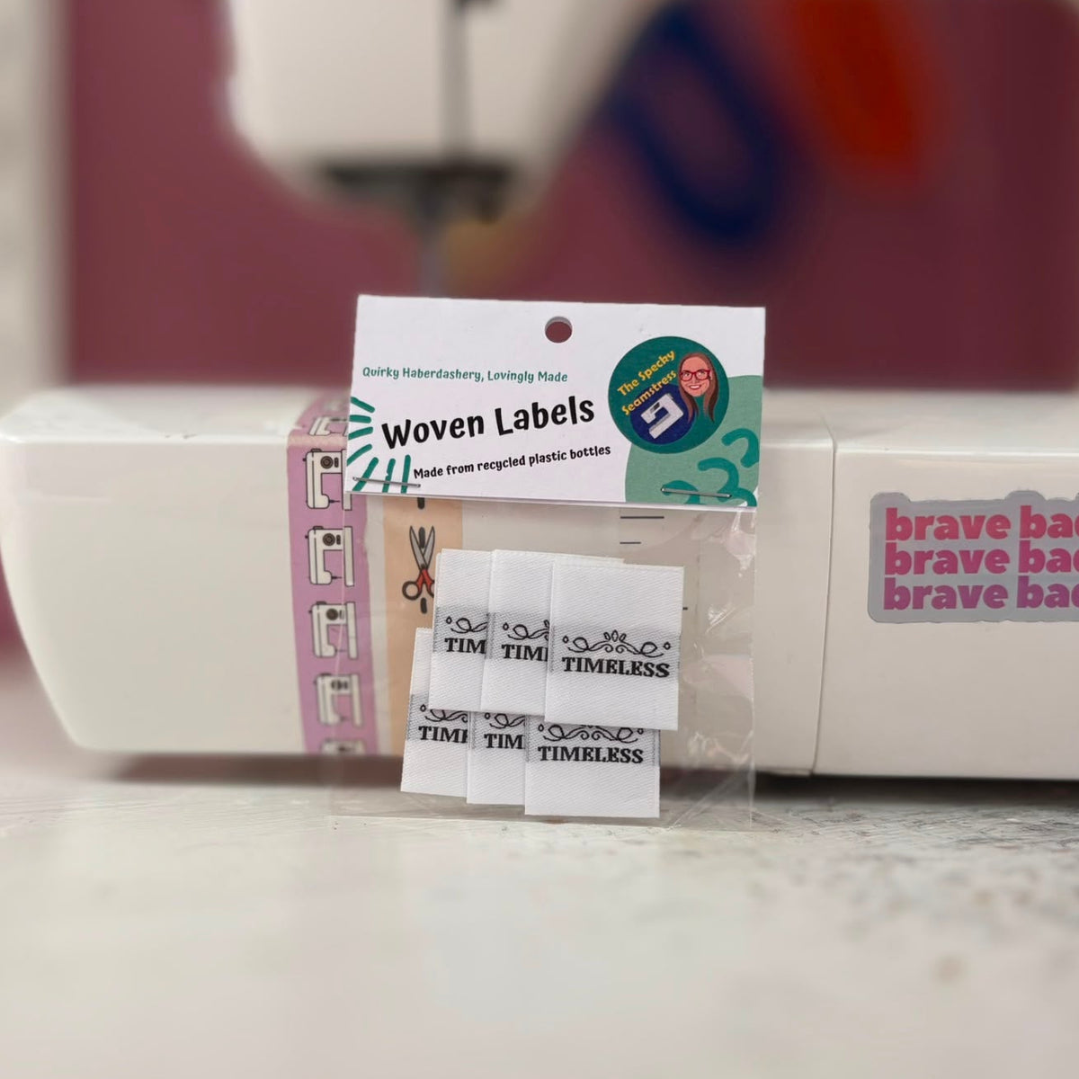 A package of labels propped up against a sewing machine; the white labels say the word Timeless in a black capitalised font. 
